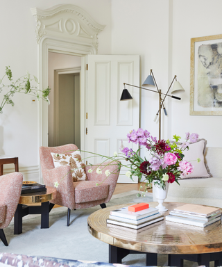 living room with pink armchair white walls and floor ligth and coffee table with vase of pink flowers and plaster detail above door