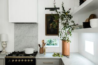 Close up of kitchen countertop with white marble detailing, white walls and framed still life artwork with lamp over the top