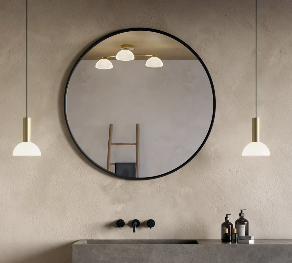 a bathroom with limewash walls with modern lighting and a large round mirror