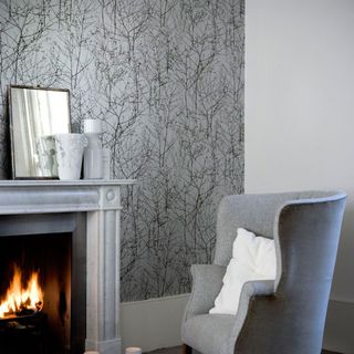 fireplace and grey chair with tree print wallpaper