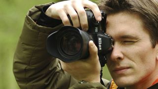 Photographer using a Nikon F100 to take pictures in a bluebell wood in England