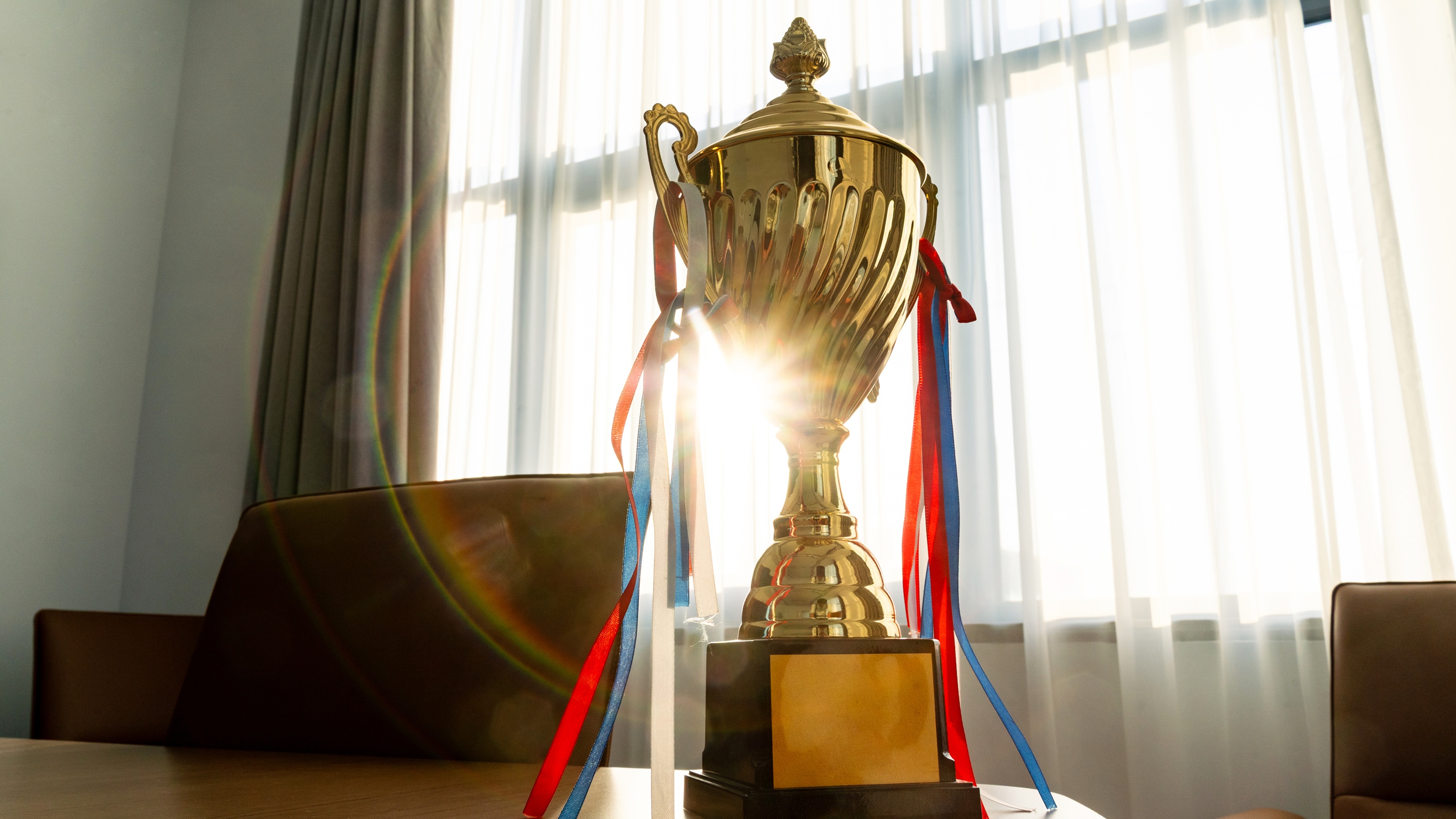 A trophy with ribbons sits on a table in sunlight.