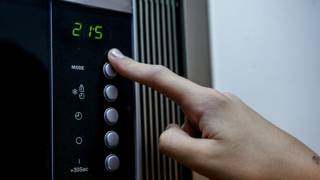 A hand touching a microwave oven&amp;#039;s controls