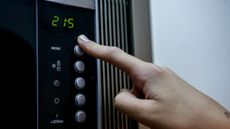 A hand touching a microwave oven's controls