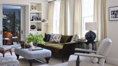 a large formal living room in New York with elegant moldings, neutral walls, doorway bookcases, olive green velvet couch, small accent chairs and an ottoman