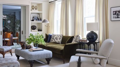 a large formal living room in New York with elegant moldings, neutral walls, doorway bookcases, olive green velvet couch, small accent chairs and an ottoman