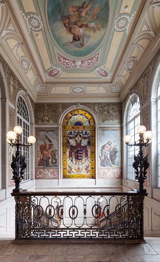 Staircase in the Palacio Chiado. Beautiful iron fence, with light fixtures at the top. The walls are decorated with elaborate frescoes and stained glass windows.