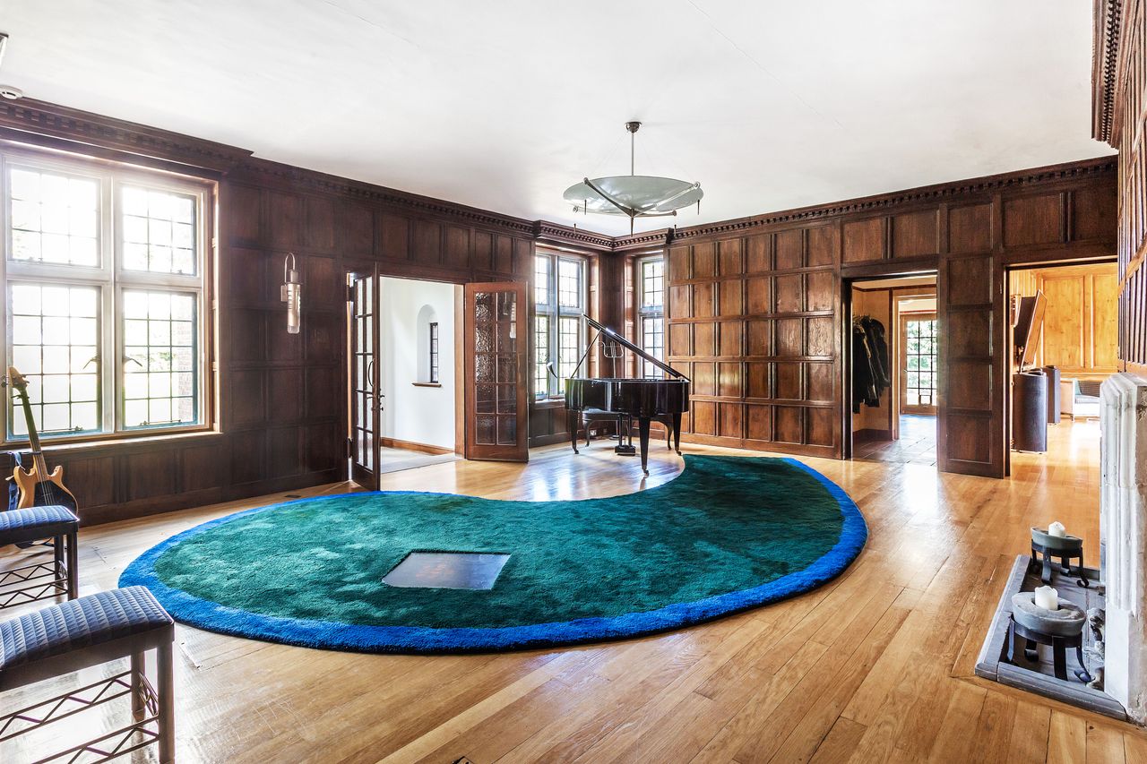 A wooden lounge with a piano and large tear drop shaped carpet