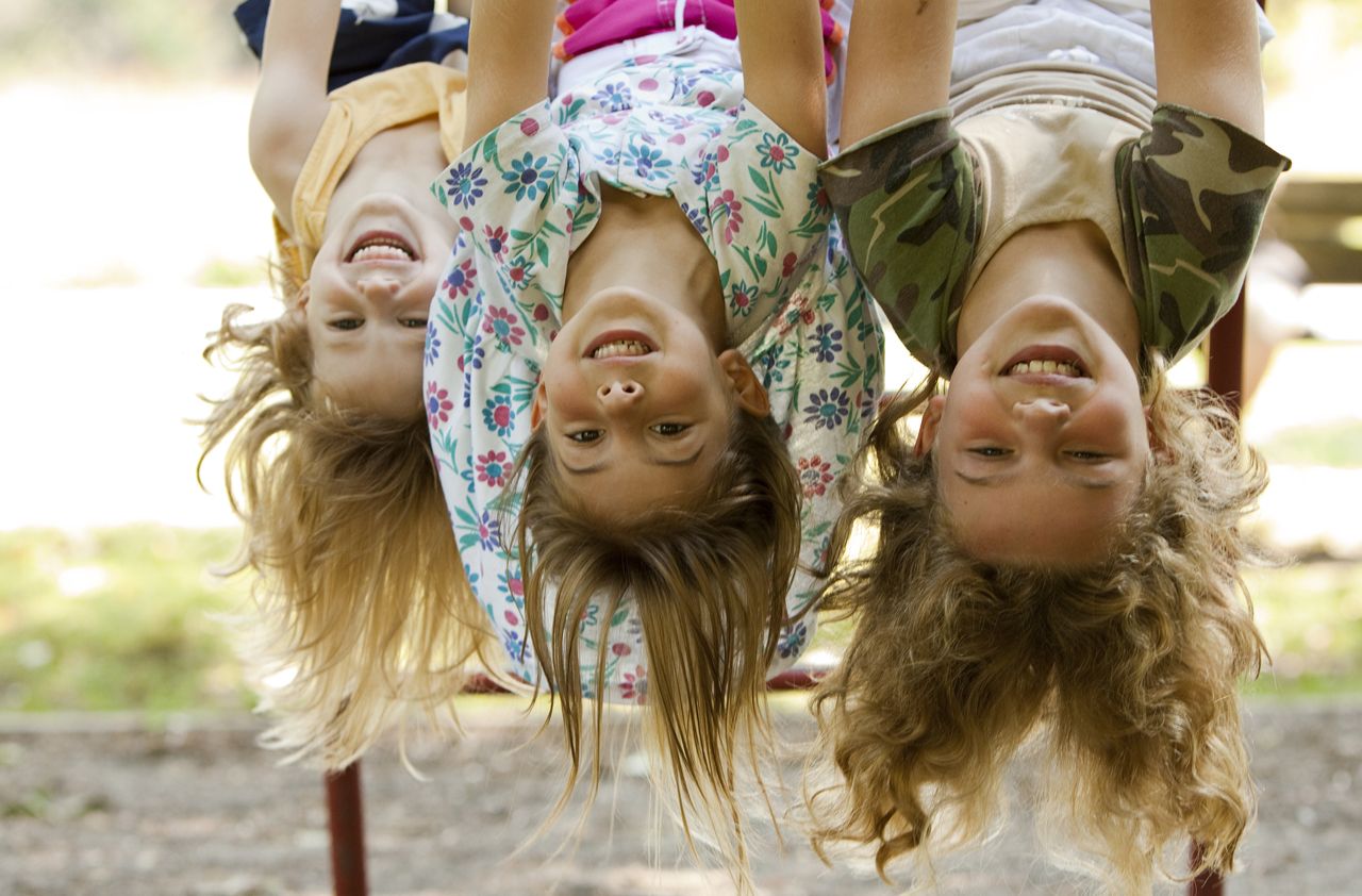 Three sisters hang upside down at playground.