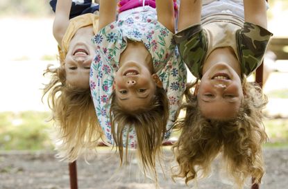 Three sisters hang upside down at playground.