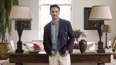 Jake Arnold standing up and looking to camera waearing a blue blazer and between two lamps