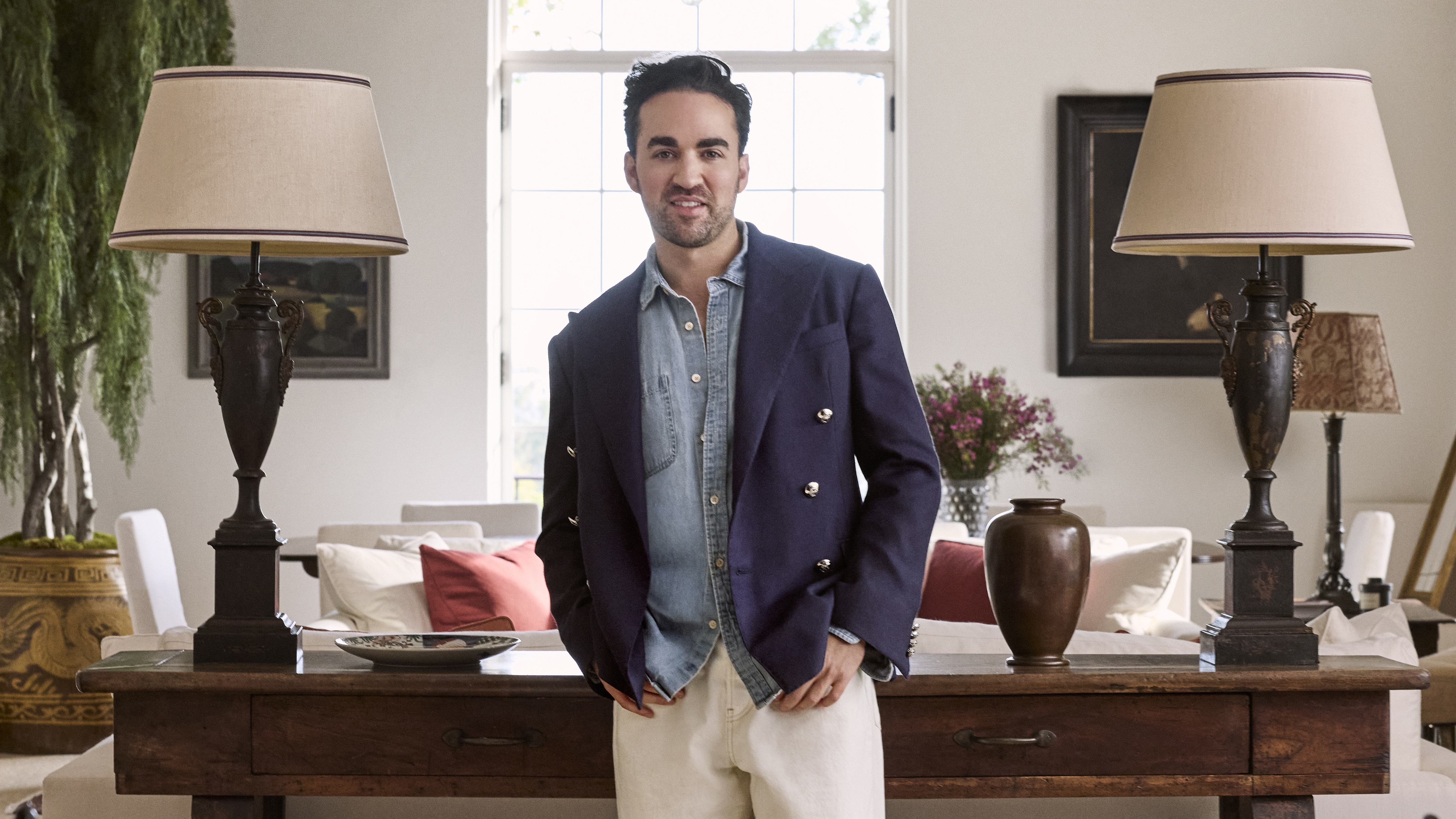 Jake Arnold standing up and looking to camera waearing a blue blazer and between two lamps