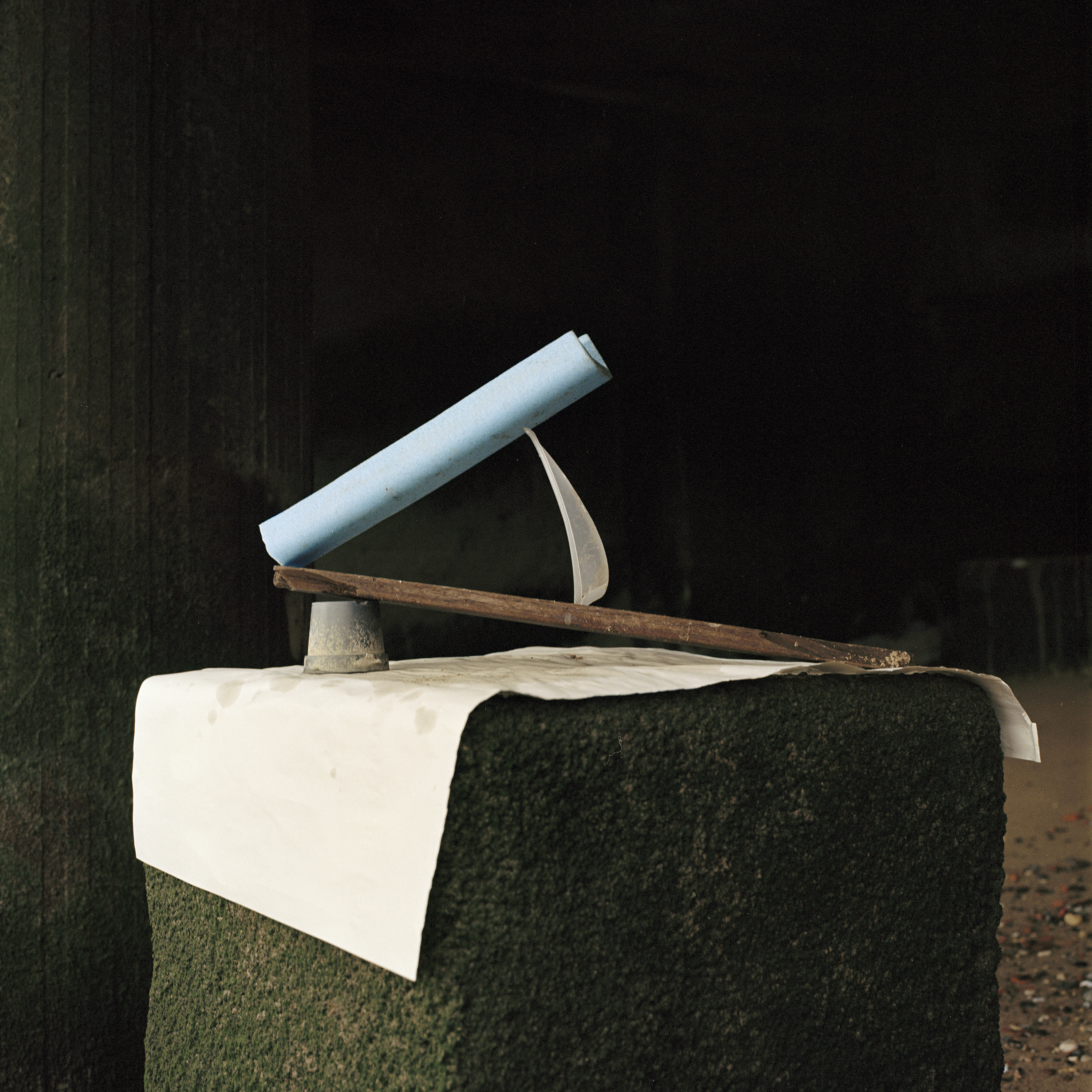 A flower pot, a piece of wood, a piece of plastic and a piece of blue Styrofoam stacked on top of each other on a sheet of paper on an algae covered stone