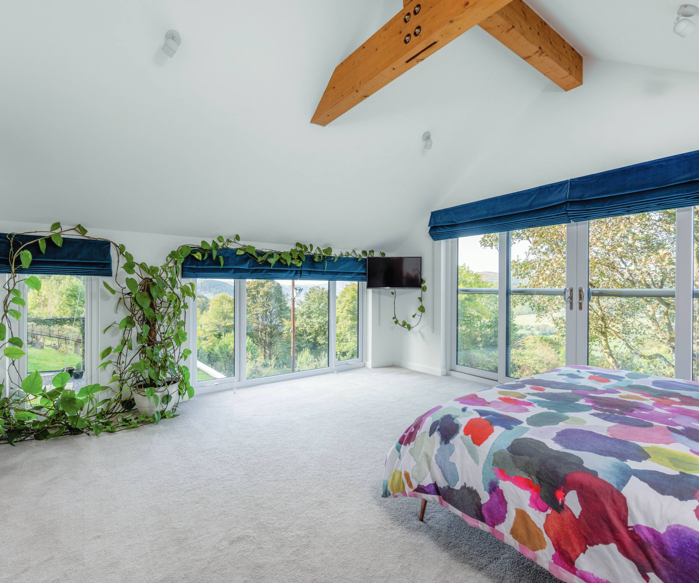 Light and open airy bedroom with vividly coloured bed linen, navy blue blinds and full-height windows and a grey carpet