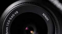 Close-up of a Nikon lens displaying specifications: 18-55mm, f/3.5-5.6G VR, highlighting its design and lens elements against a dark background