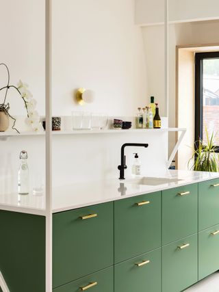 A kitchen with green drawers and copper handles