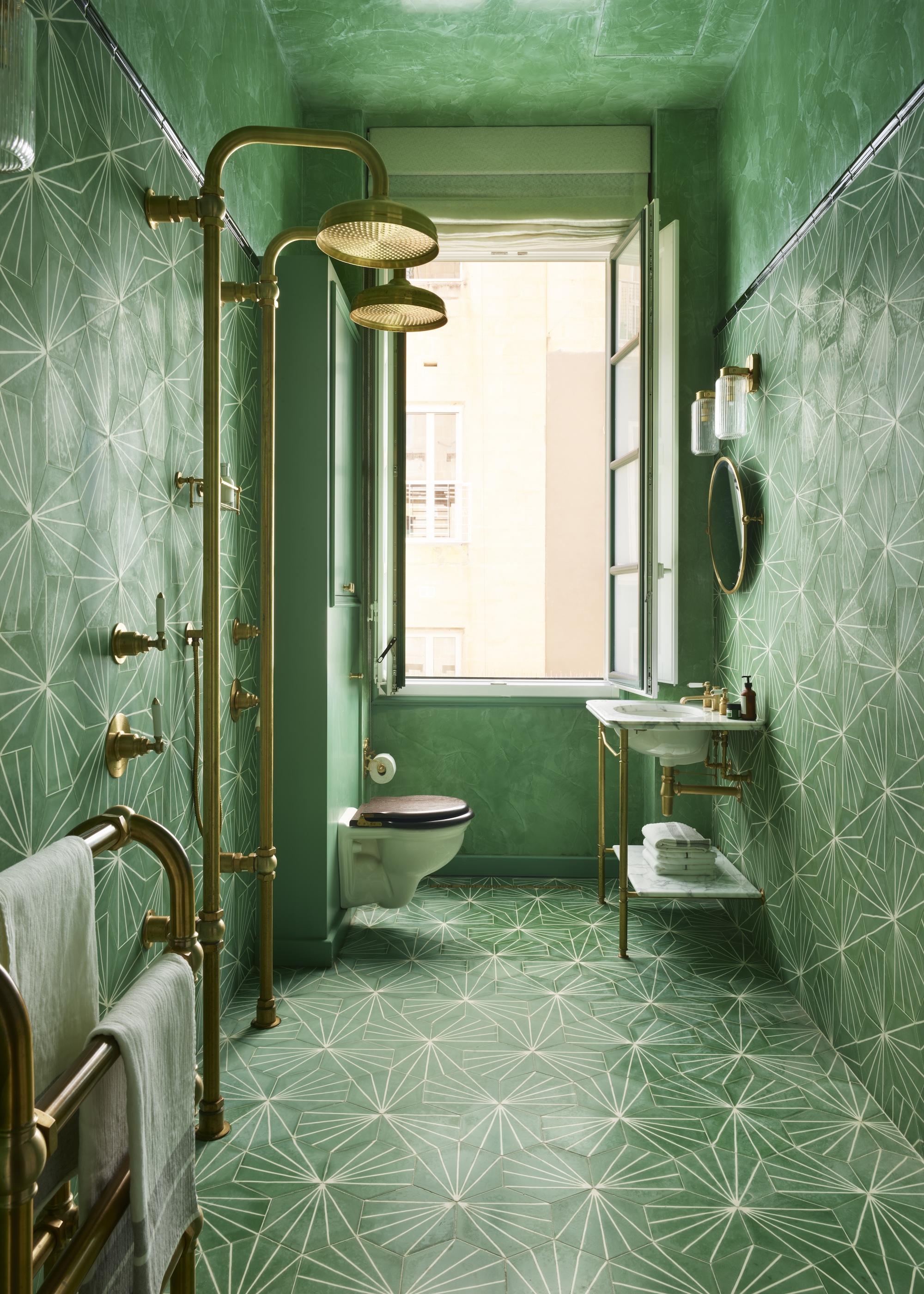 A bathroom-wet room covered in vibrant green geometric wall tiles with two vintage style brass showers