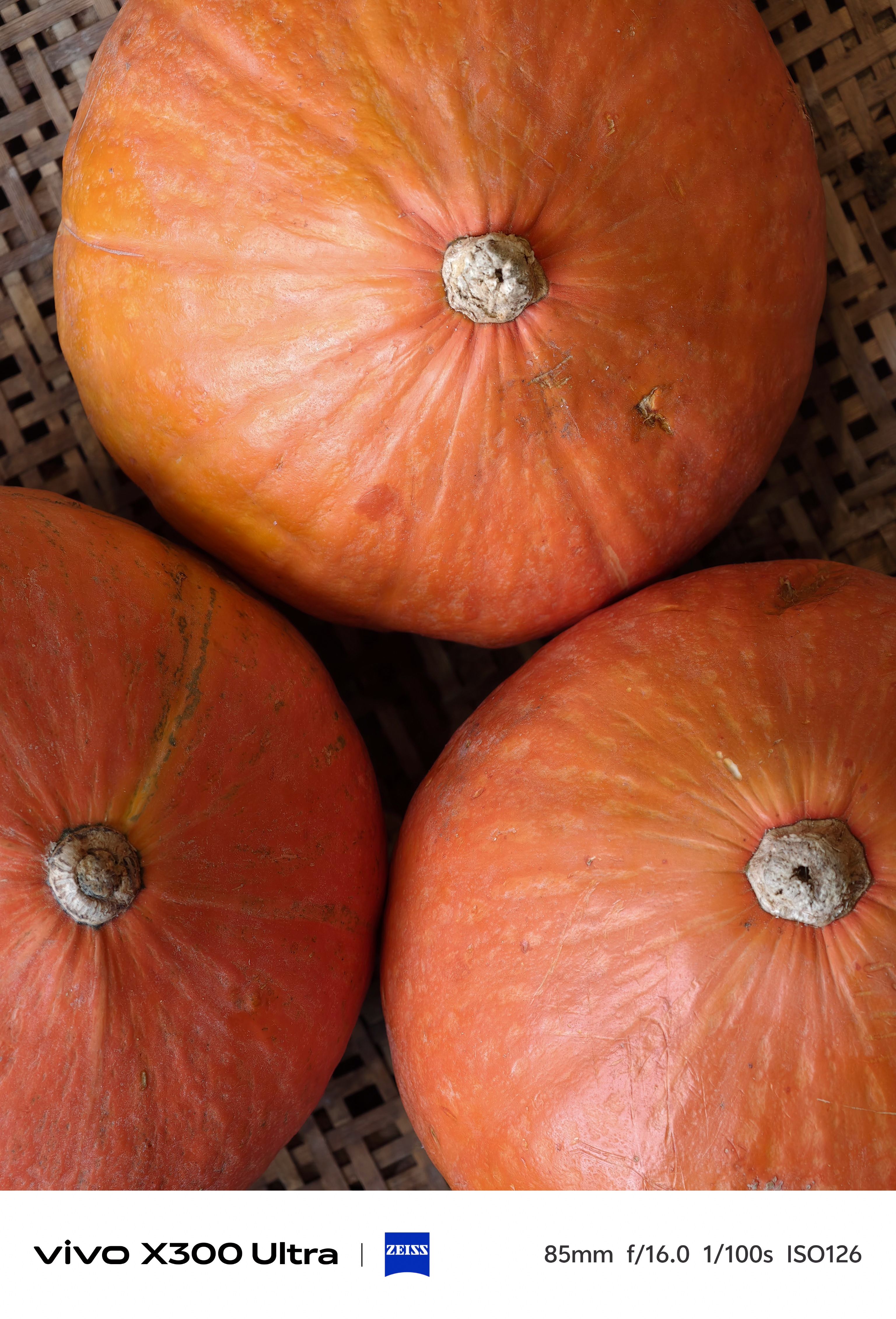 Overhead shot of three round, textured orange pumpkins arranged closely together against a dark, woven wicker background.