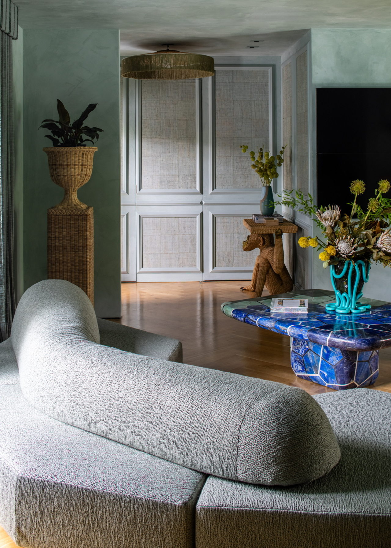 a living room with a gray sectional sofa and bold blue marble coffee table with accent pieces and limewashed walls in a pale green/blue color