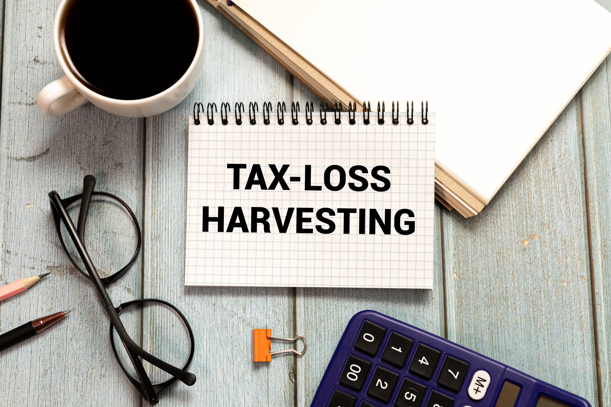 Notepad that says &quot;tax-loss harvesting&quot; on a desk with coffee, glasses, calculator, and other items