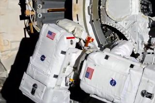 NASA astronauts Bob Behnken (at left) and Chris Cassidy work to scrape away debris from the end cone of the Tranquility node to prepare the International Space Station for the addition of its first commercial airlock during a July 21, 2020 spacewalk.