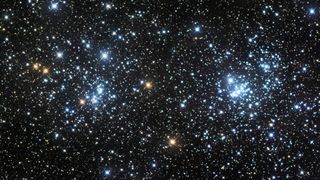 a star filled image is dominated by two distinctly bright and dense regions of stars shining white/blue. Some more yellow stars also shine close to the clusters.