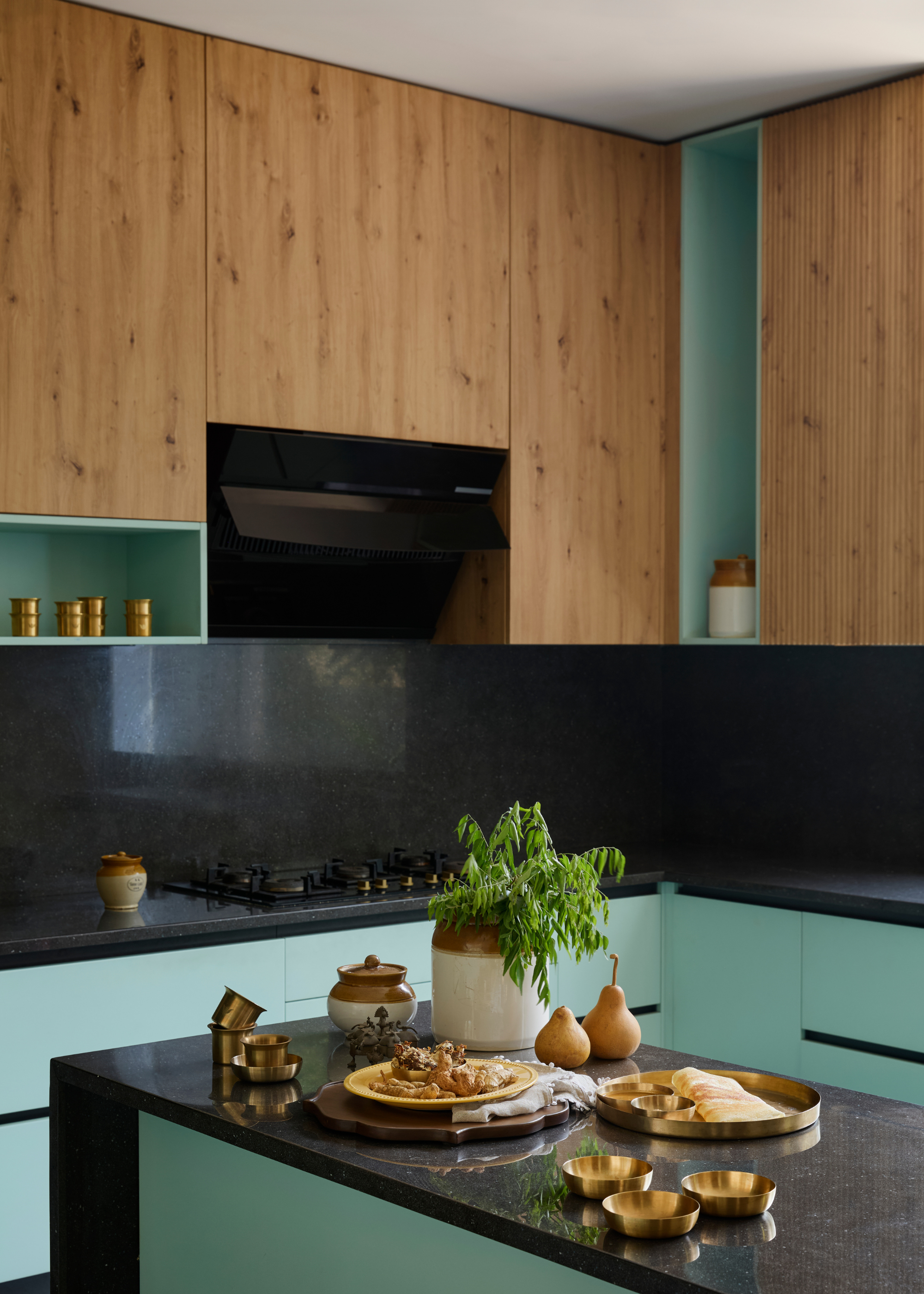 An Indian kitchen with wooden cabinets, light teal accents and a small island