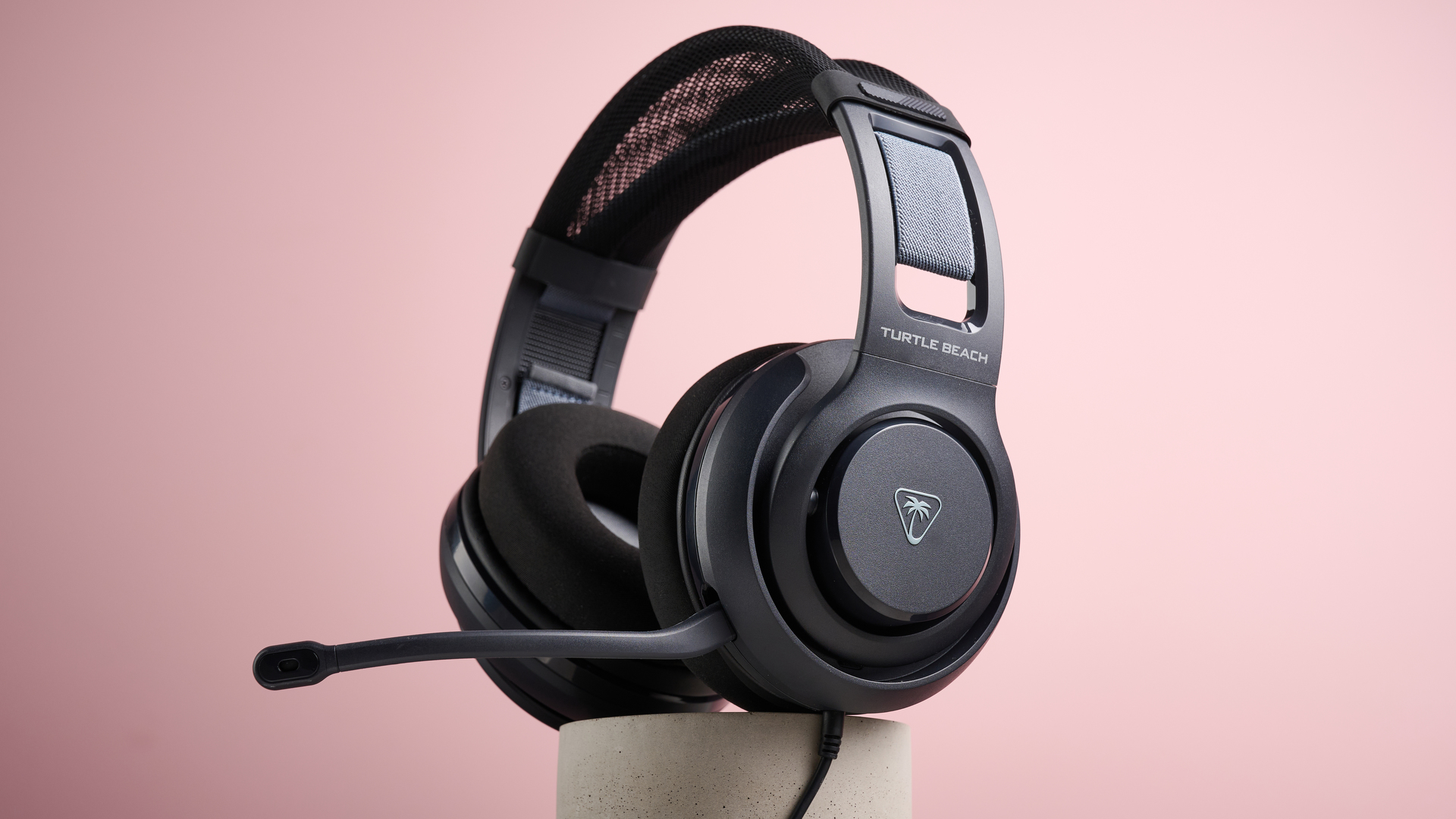 The Turtle Beach Atlas 200 sat on top of a cylinder, with the mic folded out, in front of a pink background.