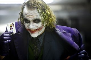 heath ledger as the joker holding up a card in a the dark knight film still