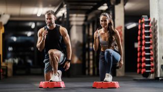 Muscular couple performing a step aerobics workout in the gym performing a lunge on the step