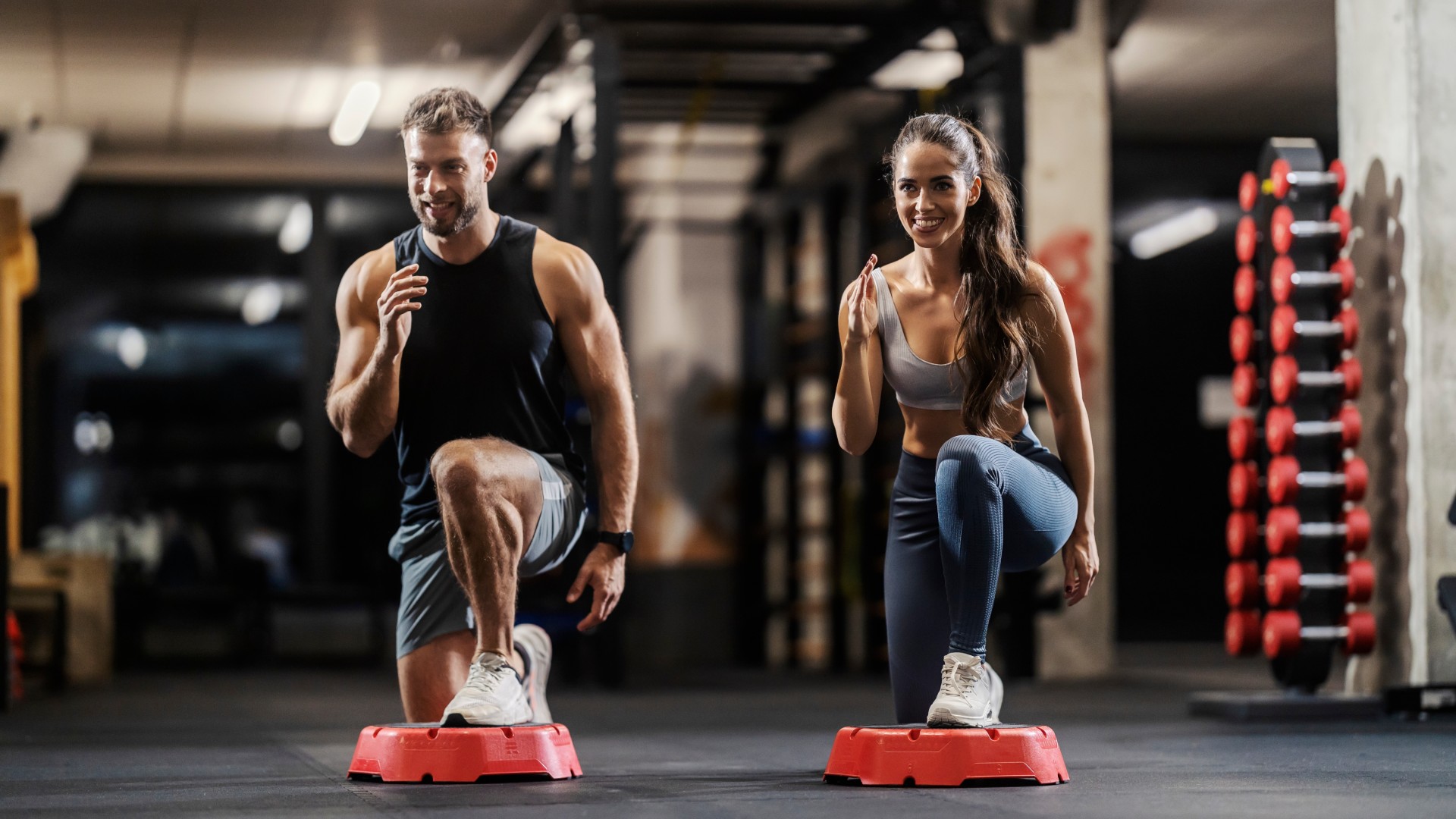 Muscular couple performing a step aerobics workout in the gym performing a lunge on the step