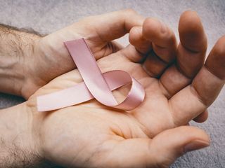 A hand holding a pink breast cancer awareness ribbon.