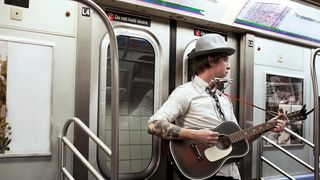 A guitarist busks on a New York City subway car