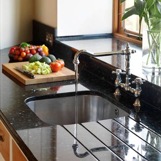 sink area with black worktop and chopping board with veggies