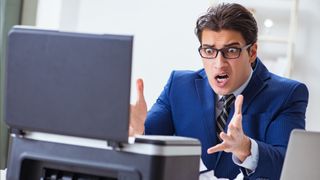 A distressed man looking at a broken printer in panic