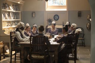 A group of Regency-era servants have tea at a dining table, in 'Bridgerton' season 4.