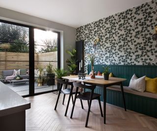 wallpapered wall with a green botanical print, built in banquette style seating and dining table with extra chairs