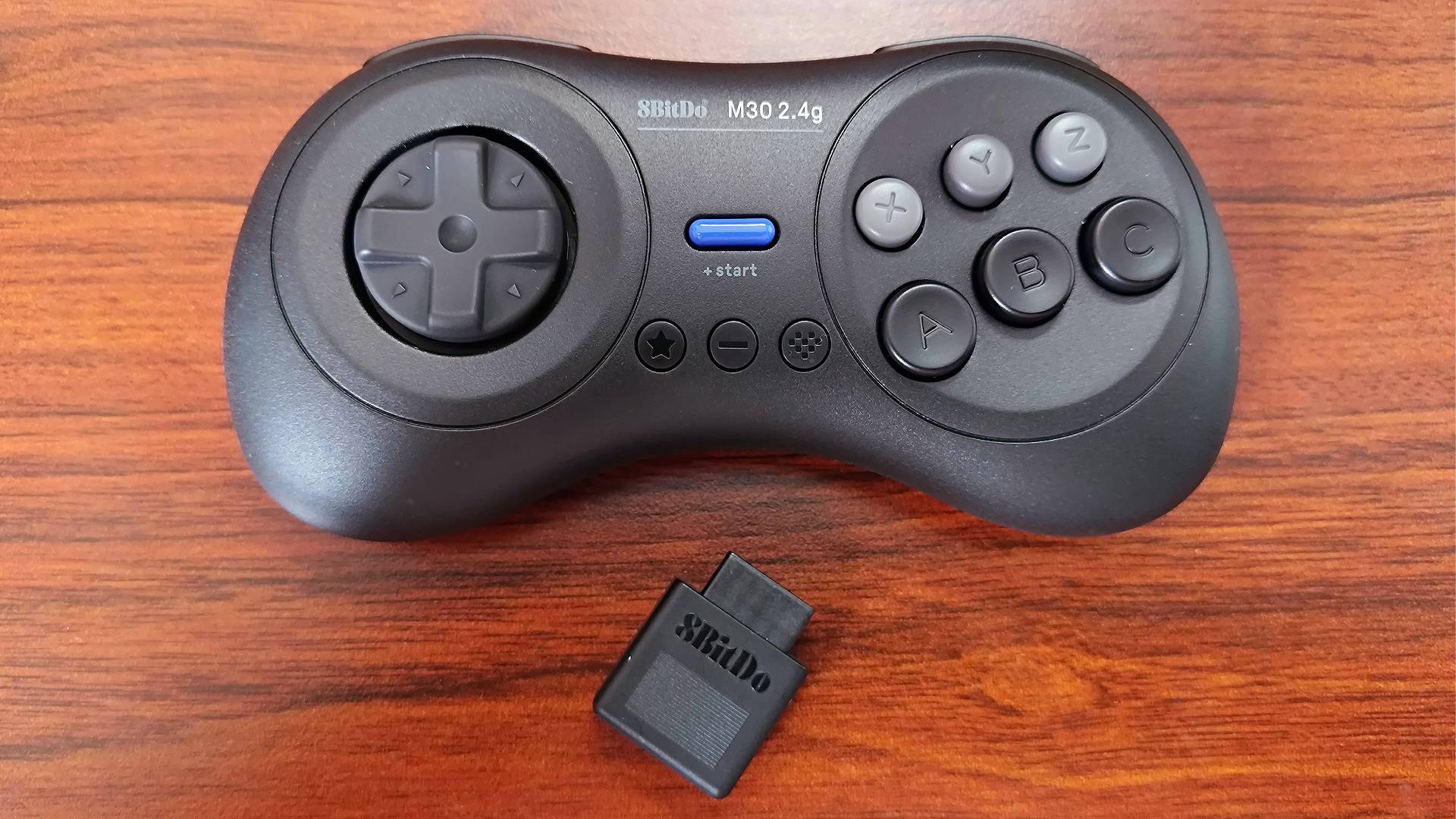 8Bitdo M30 Sega Mega Drive/Genesis 23.4Ghz Wireless controller on woodgrain desk with adapter sitting under gamepad.