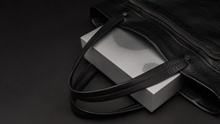 Nocs Lab Monolith Aluminum speaker poking out from a leather bag, showing that the speaker is small enough to fit in a large-sized shoulder bag
