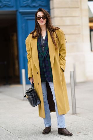 a street style influencer wearing a yellow coat and straight leg jeans
