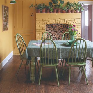 A yellow-painted dining room with a green table and matching chairs and natural wooden floor