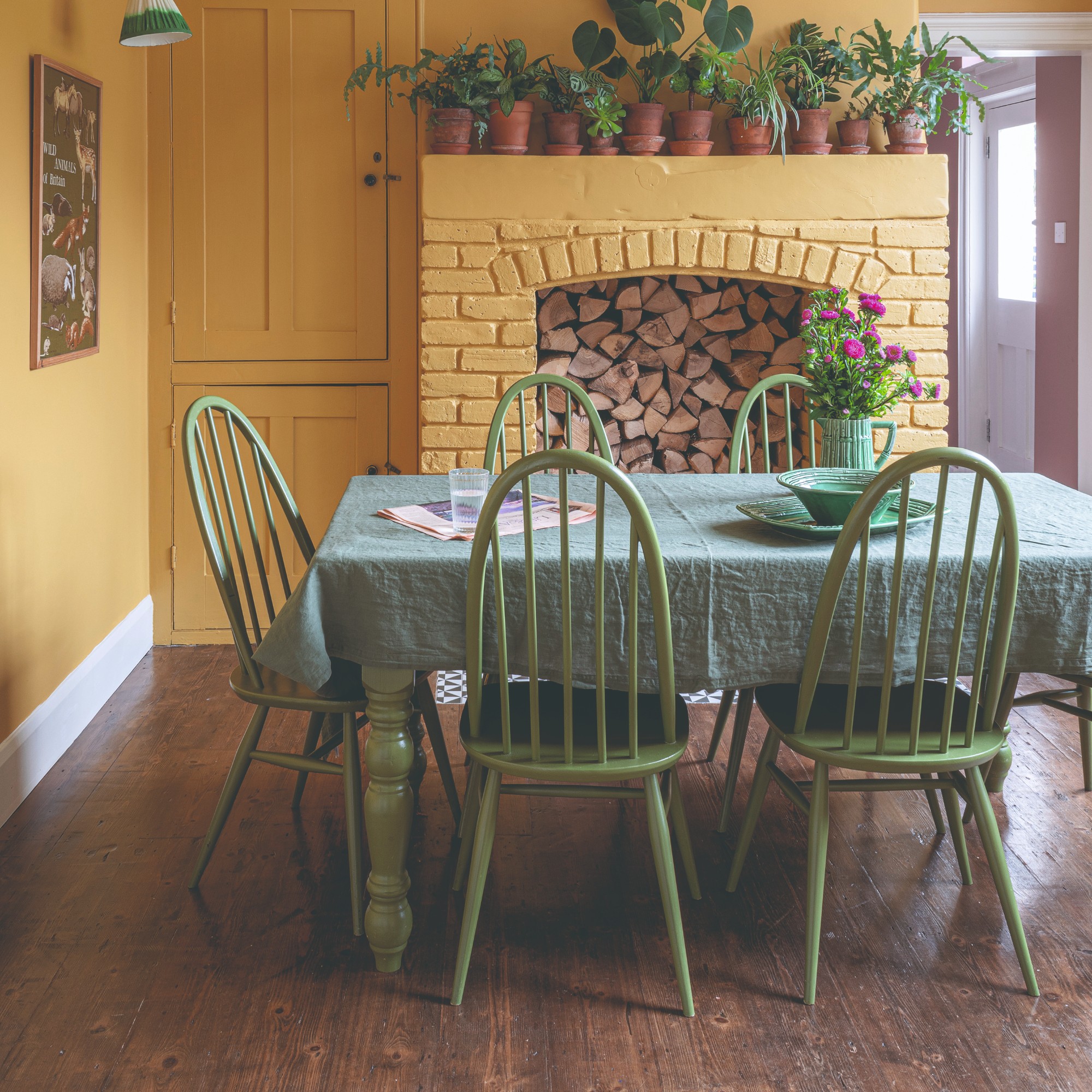 Un comedor pintado con amarillo con una mesa verde y sillas a juego y piso de madera natural