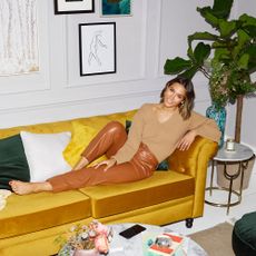 Frankie Bridge laying on a mustard yellow sofa in a white living room.