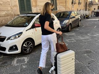 Woman wearing white pants and holding a suitcase