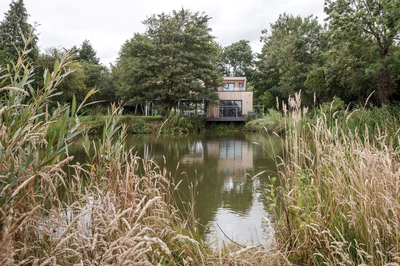 A self build timber cladded home seen over the pond from a distance