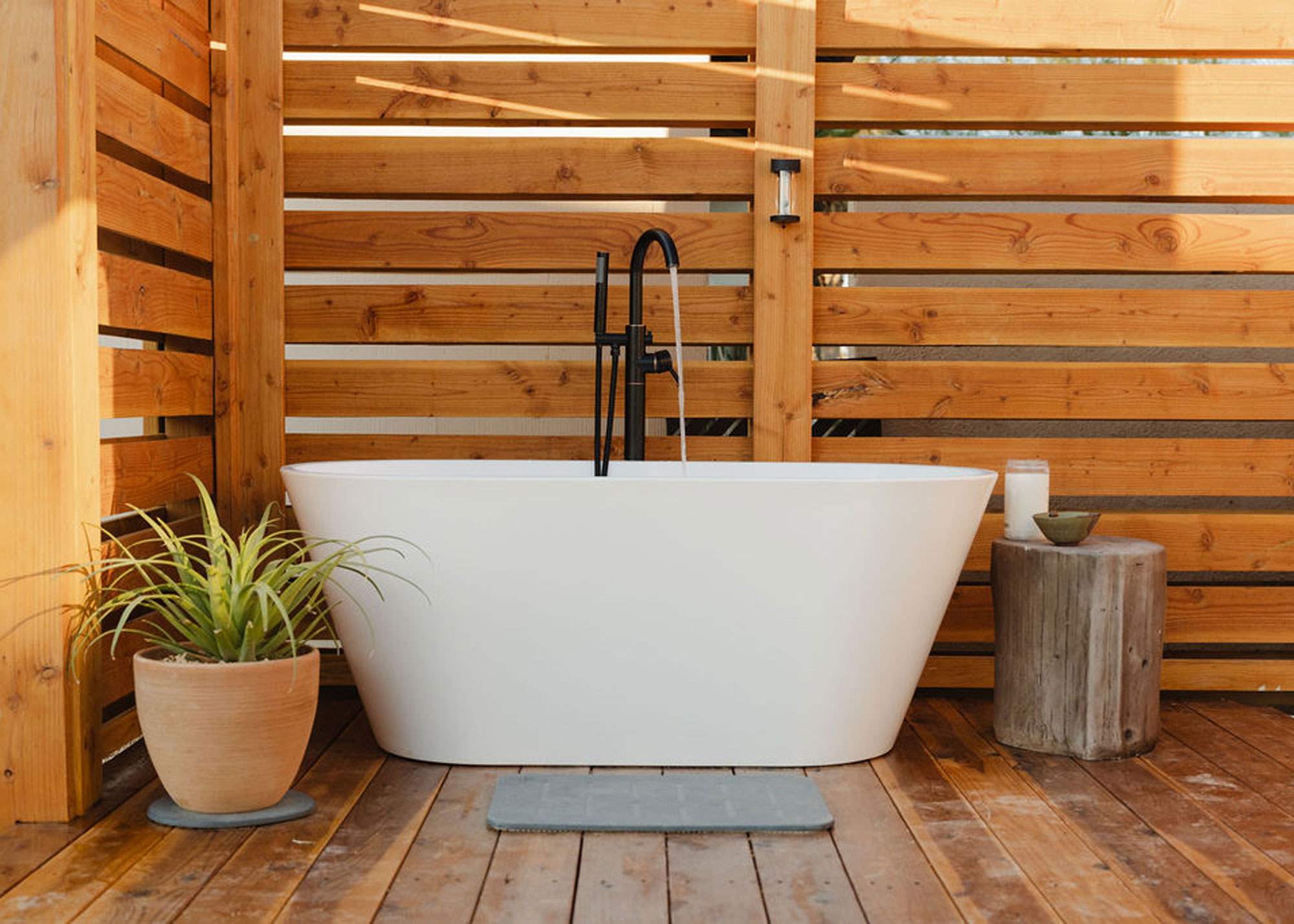 outdoor bathroom on deck with a bath tub in the middle as well as a side table and plant pot.