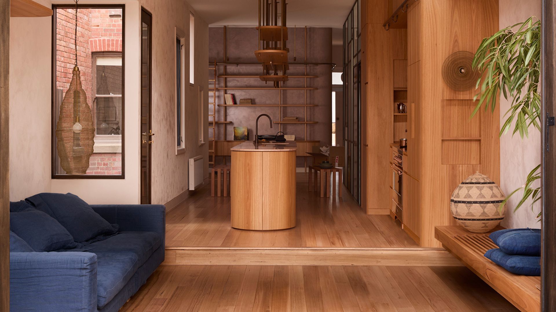 An airy open living and kitchen space with a wooden bench, a blue sofa, a wood island, and storage shelves