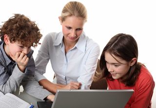 A teacher and two kids share a laptop computer