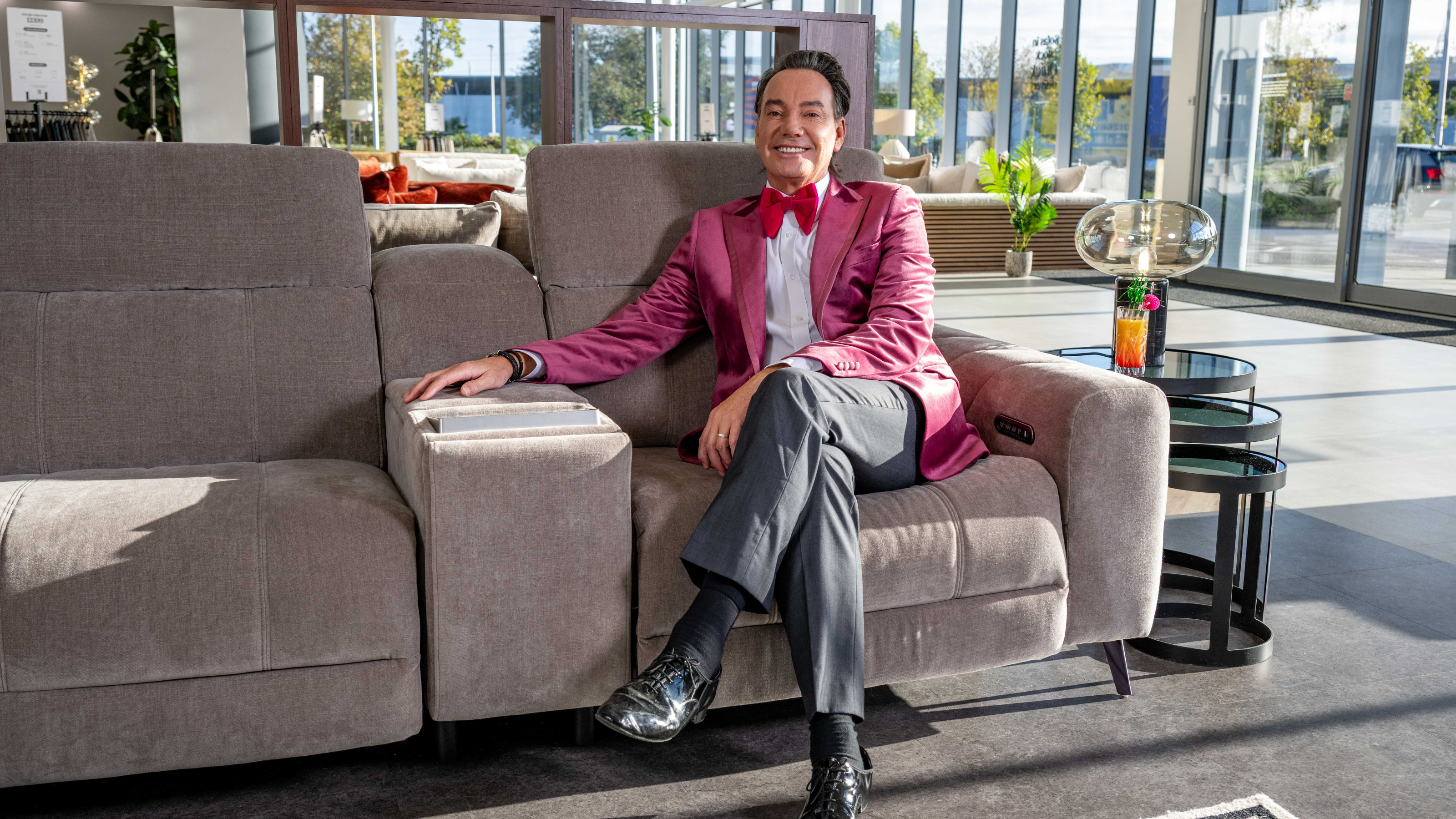 Craig Revel Horwood sat on a grey sofa in the Sofology show room.