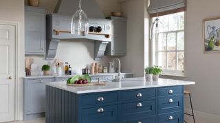 A classic kitchen with a navy blue island featuring shaker-style drawers and silver cup handles. A light quartz countertop holds fresh vegetables and a modern sink with a curved faucet.